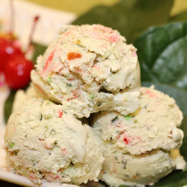 Three scoops of Kwality Norwood ice cream with colorful fruit pieces, garnished with cherries and green leaves.
