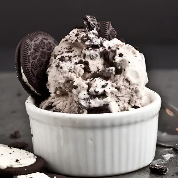 A white bowl of cookies and cream ice cream with an Oreo cookie on the side.