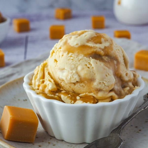 A scoop of Kwality Norwood caramel ice cream in a white bowl, with caramel squares scattered around.