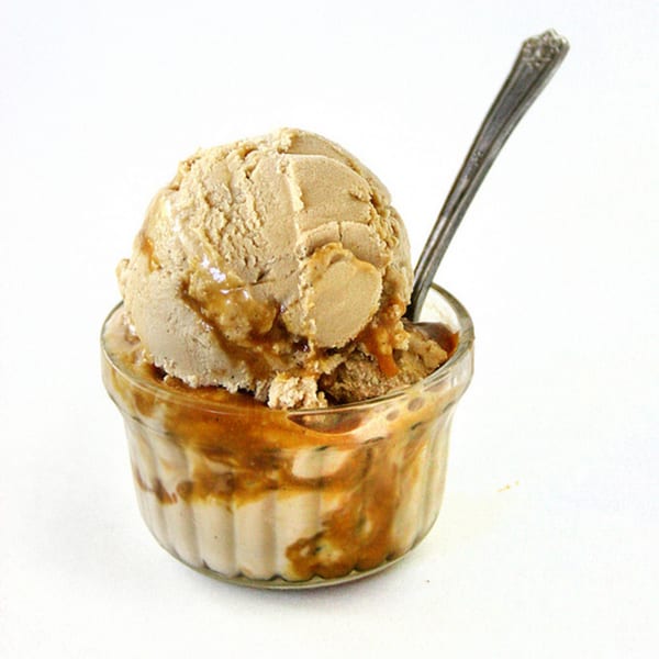 A scoop of Kwality Norwood ice cream with caramel drizzle in a glass cup with a spoon.