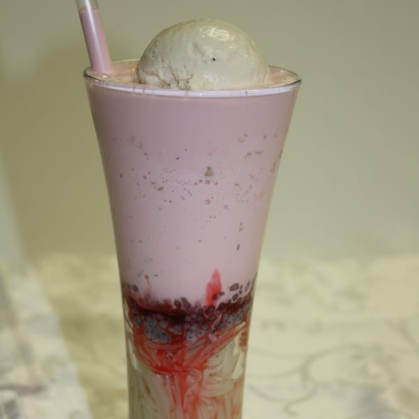 A tall glass of pink Falooda with a scoop of vanilla ice cream and a straw.