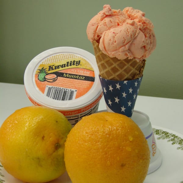 Kwality Mumtaz orange-pineapple ice cream in a waffle cone and a tub, with two oranges.